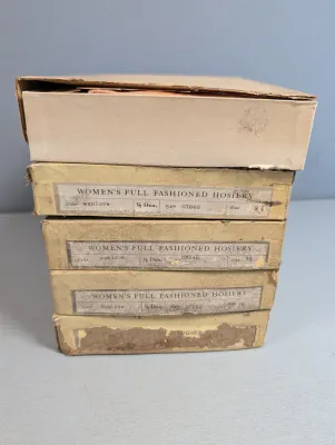Sale Photo Thumbnail #422: Stack of vintage boxes of women's full-fashioned hosiery in size 9.5 and color sunlove, showing some wear to the cardboard packaging.
