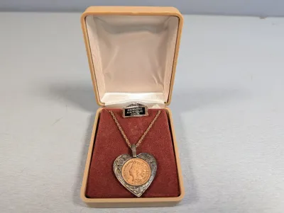 Sale Photo Thumbnail #406: Heart-shaped pendant necklace featuring a 1906 Indian Head penny set in a silver-tone bezel, displayed in its original 'Genuine Antique Coin' presentation box.