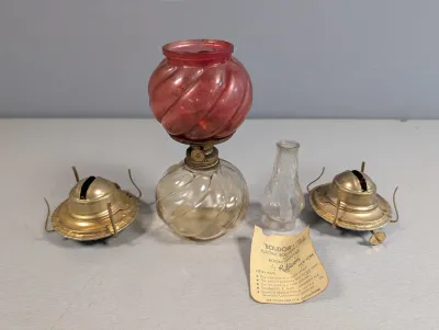 Sale Photo Thumbnail #393: Vintage Rubicon 'Boudoir-Lite' electric room perfumer lamp with swirled cranberry and clear glass, accompanied by extra brass burners, a clear glass chimney, and an original paper tag.