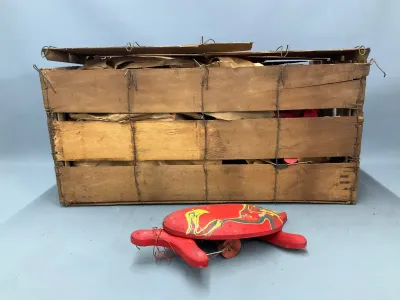 Sale Photo Thumbnail #156: Vintage red painted wooden turtle pull toy, featured in front of a rustic wire-bound wooden produce crate filled with brown packing paper.