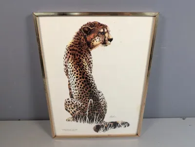 Sale Photo Thumbnail #451: Framed wildlife art print depicting a seated cheetah, housed in a thin gold-tone metal frame.