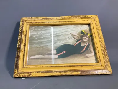 Sale Photo Thumbnail #147: Vintage framed hand-tinted photograph of a woman in an early 20th-century bathing suit, housed in a distressed yellow wooden frame.