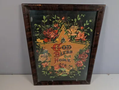 Sale Photo Thumbnail #297: Antique framed Victorian motto print reading 'God Bless Our Home' with ornate floral illustrations and a gold star design, housed in a dark wood frame.