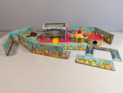 Sale Photo Thumbnail #304: Vintage Superior Space Port lithographed tin playset, featuring a central space drome structure and colorful sci-fi city backdrop panels.