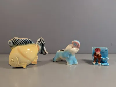 Sale Photo Thumbnail #202: Trio of vintage ceramic novelties and planters, including a yellow fish, a blue elephant planter, and a novelty monkey on a toilet figurine reading 'Be My Guest.'