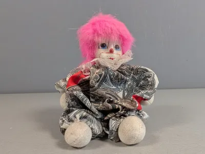 Sale Photo Thumbnail #387: Vintage soft-bodied clown doll featuring pink fuzzy hair, painted facial features, and a patterned fabric ruffled outfit.