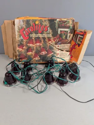 Sale Photo Thumbnail #432: Vintage Carolites musical Christmas bell lights with original packaging and power adapter, featuring red translucent bell-shaped covers on green wiring.