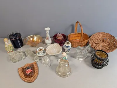 Sale Photo Thumbnail #417: Collection of decorative tabletop knickknacks and collectibles, including carnival glass, porcelain figurines, woven baskets, and a wall-mounted bear head plaque.