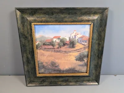 Sale Photo Thumbnail #447: Framed oil painting depicting a rural European landscape with red-roofed cottages, set in a wide, mottled dark green and gold wooden frame.