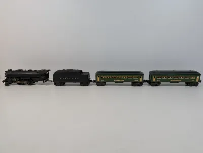 Sale Photo Thumbnail #119: Vintage Lionel pre-war O-gauge train set featuring a black steam locomotive, Lionel Lines coal tender, and two green Pullman passenger cars.