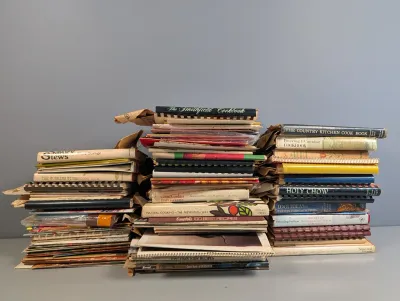 Sale Photo Thumbnail #286: Large stack of vintage cookbooks and recipe booklets featuring mid-to-late 20th-century titles including 'The Smithfield Cookbook' and 'Holy Chow'.