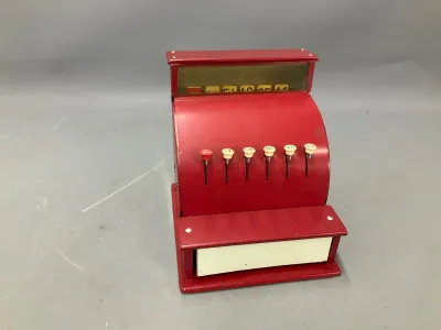 Sale Photo Thumbnail #155: Vintage red metal toy cash register featuring plastic key pop-ups and a cash drawer, showing minor paint wear consistent with age.
