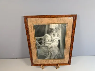 Sale Photo Thumbnail #176: Framed black-and-white portrait print of a mother and child seated by a window, housed in an oak wood frame with a patterned mat board.