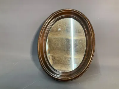Sale Photo Thumbnail #143: Vintage oval wall mirror with a molded dark wood frame, showing light wear and scuffing along the edges.