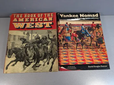 Sale Photo Thumbnail #270: Two hardcover vintage books with dust jackets, including "The Book of the American West" and David Douglas Duncan's "Yankee Nomad". Both show light shelf wear along the edges.