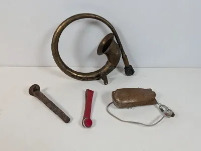 Sale Photo Thumbnail #106: Collection of vintage auto parts including a coiled brass horn, rusted metal hardware, a red strap reflector, and a pedal switch.