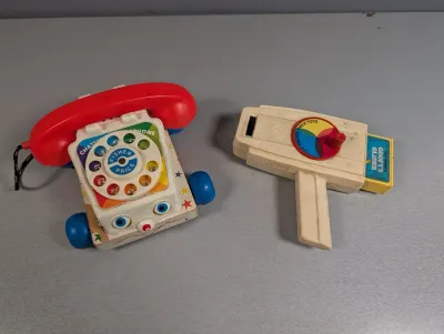 Sale Photo Thumbnail #383: Vintage Fisher-Price toy set featuring a classic Chatter Telephone pull toy and a Movie Viewer with a Walt Disney Goofy's Glider cartridge.