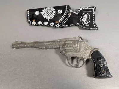 Sale Photo Thumbnail #315: Vintage Hubley Kit Carson die-cast cap gun with a embossed western design and a black faux leather holster.