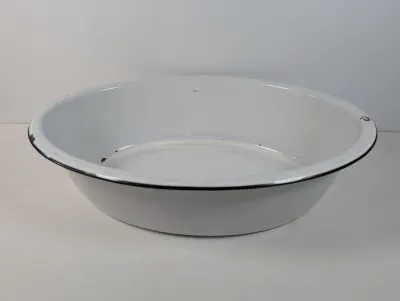Sale Photo Thumbnail #134: Vintage white enamelware wash basin with a black trim rim, showing light wear and minor chips.