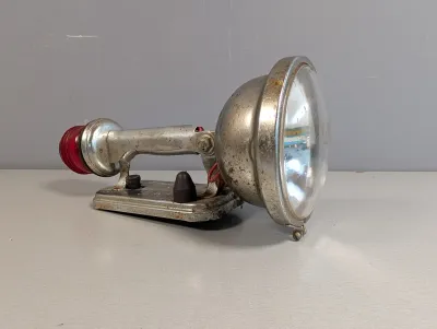 Sale Photo Thumbnail #247: Vintage Big Beam handheld portable spotlight with a red rear lens and metal casing, showing age-appropriate patina and surface rust.
