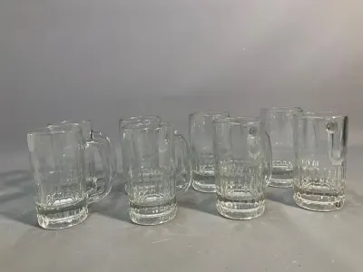 Sale Photo Thumbnail #56: Set of seven clear glass beer mugs featuring textured panel bases and sturdy handles, all in good condition.