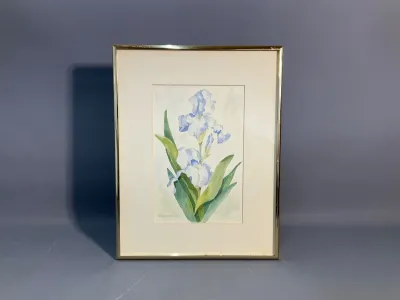 Sale Photo Thumbnail #139: Framed watercolor painting depicting pale blue irises, signed by the artist in the lower left corner and set in a polished brass-tone metal frame.