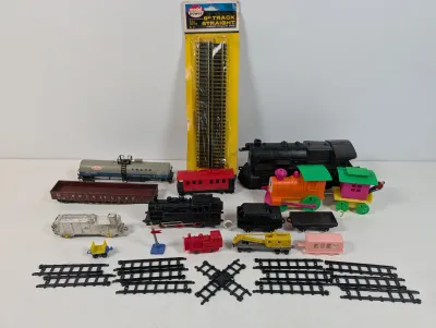 Sale Photo Thumbnail #117: Assorted vintage toy trains and track pieces, including a packaged Model Power HO scale straight track set, plastic locomotives, passenger cars, freight cars, and layout accessories.