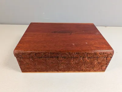 Sale Photo Thumbnail #242: Hand-carved wooden trinket box featuring a floral pattern along the sides and a personalized inscription on the smooth lid.
