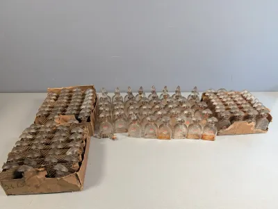 Sale Photo Thumbnail #370: Large collection of vintage miniature glass perfume bottles with decorative stoppers, displayed individually and in original cardboard storage trays.