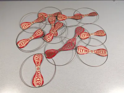 Sale Photo Thumbnail #384: Collection of vintage 'Atomic Flying-O-Saucer' wire and tin litho flying toys, featuring red and white graphics.