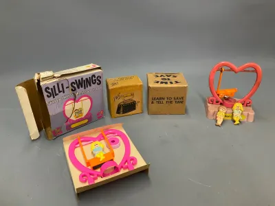 Sale Photo Thumbnail #347: Collection of vintage Silli-Swings kinetic novelties and miniature desk items with original packaging, including heart-shaped swing toys and a miniature steam iron sharpener.