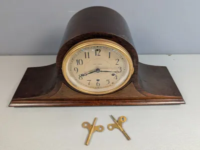 Sale Photo Thumbnail #37: Vintage Seth Thomas mahogany mantle clock featuring a brass-bezeled dial with Arabic numerals and two winding keys.