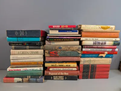 Sale Photo Thumbnail #265: Large collection of vintage hardcover and paperback books arranged in three stacks, featuring various fiction and non-fiction titles from the mid-20th century.