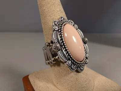 Sale Photo Thumbnail #4: Southwestern-style ring featuring a smooth, peach-colored oval cabochon set in an ornate, antiqued silver-tone scalloped border with an elastic stretch band.