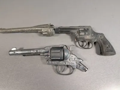Sale Photo Thumbnail #318: Trio of vintage die-cast metal toy cap guns, including a Trooper model and scroll-engraved revolvers, showing mid-century play wear.