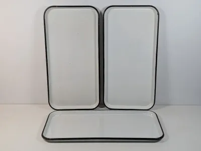 Sale Photo Thumbnail #131: Set of three vintage white enamelware rectangular trays featuring black trim around the edges.