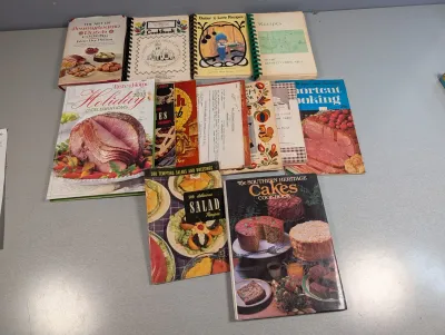 Sale Photo Thumbnail #240: Collection of vintage and modern cookbooks and recipe booklets, including mid-century community cookbooks and spiral-bound editions.
