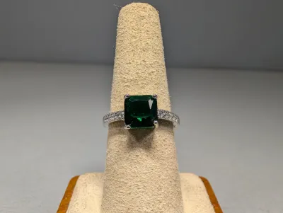 Sale Photo Thumbnail #7: Emerald-cut dark green gemstone ring in a silver-tone band with paved accent stones on the shoulders, displayed on a suede cone.