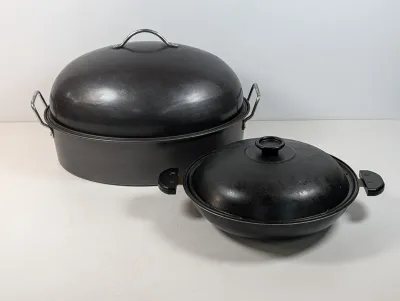 Sale Photo Thumbnail #132: Two vintage dark gray cookware pieces with matching lids, including a large high-domed oval roasting pan and a round covered skillet.