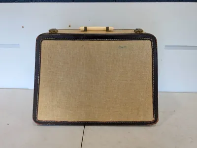 Sale Photo Thumbnail #491: Vintage hard-shell luggage case with a beige textured body, dark brown trim with contrast white stitching, brass latches, and a cream-colored top handle.