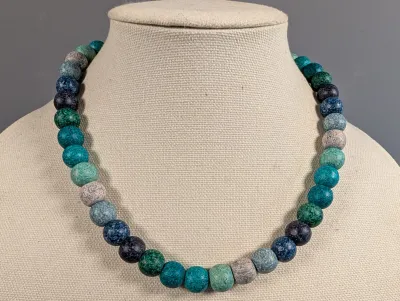 Sale Photo Thumbnail #3: Chunky beaded strand necklace featuring round, textured beads in alternating tones of teal, turquoise, navy, and cream, displayed on a fabric jewelry bust.