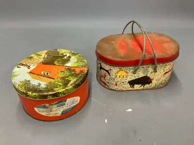 Sale Photo Thumbnail #363: Pair of vintage oval tin containers, including a Continental Assortment tin with a scenic lid and a red-topped basket-style tin with cave art graphics and a wire handle.