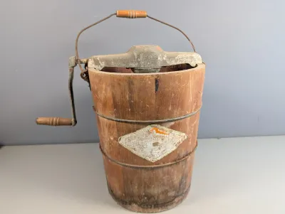 Sale Photo Thumbnail #28: Vintage hand-crank ice cream maker featuring a stenciled wooden bucket with metal bands and a cast iron gear top.