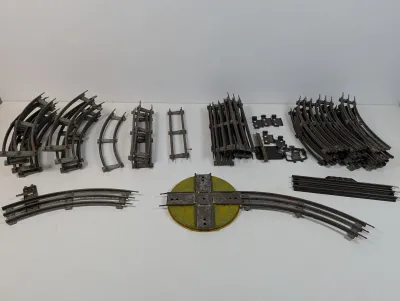 Sale Photo Thumbnail #118: Assortment of vintage Lionel 3-rail O gauge train tracks, including straight sections, curved tracks, and a 90-degree crossover intersection.