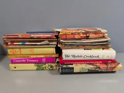 Sale Photo Thumbnail #289: Collection of vintage mid-century to late 20th-century cookbooks and recipe pamphlets stacked in two piles.