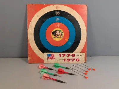 Sale Photo Thumbnail #153: Vintage 1976 US Bicentennial dartboard featuring a central buffalo graphic, complete with a set of feathered and plastic darts.
