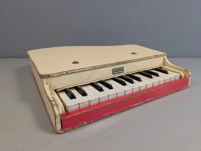 Sale Photo Thumbnail #194: Vintage off-white and red toy grand piano showing play wear and paint chipping throughout.