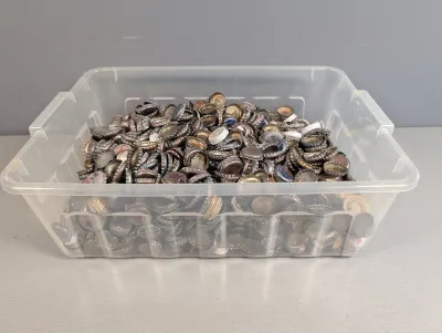 Sale Photo Thumbnail #284: Clear plastic storage container filled with a large collection of assorted vintage metal bottle caps, showing various soda and beer brands.