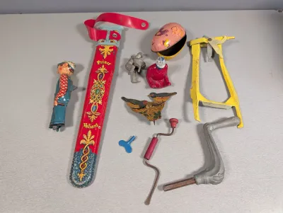 Sale Photo Thumbnail #414: Collection of vintage tin-litho wind-up toys and novelties, including a Prince Valiant sword sheath, bird figures, small figurines, and mechanical cranks.