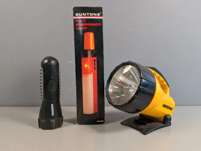 Sale Photo Thumbnail #248: Collection of vintage flashlights and portable lights, including a yellow Rayovac spotlight lantern, a black Rayovac handheld flashlight, and a boxed Suntone 5-in-1 emergency light.